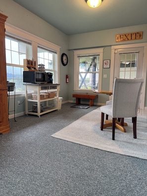 A room with a kitchen area, a dining table, a gray chair, a white rug, and an exit sign.