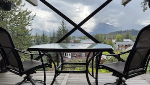 A wooden deck with a glass table and two chairs, overlooking a residential area with houses and trees. - Breathtaking mountain view, private entrance, romantic getaway (Valdez)