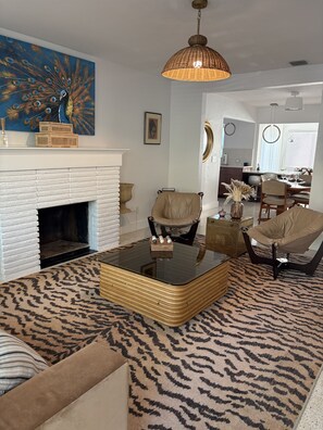 A living room with a peacock painting, a white fireplace, a glass coffee table, and a patterned rug. - Mid-Century with Outdoor Oasis (Fort Lauderdale)