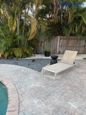 A sunlit outdoor area with a lounge chair, a small table, and a pool. - Mid-Century with Outdoor Oasis (Fort Lauderdale)