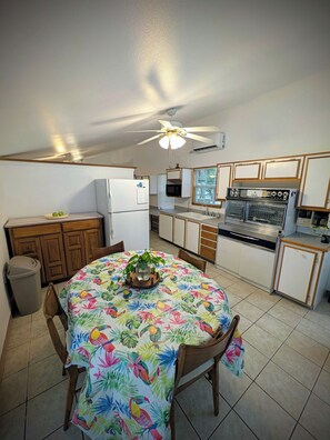 A kitchen with a dining table, chairs, a ceiling fan, and a refrigerator.
