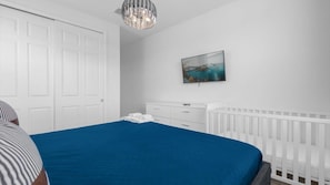 Ein Schlafzimmer mit einem großen Bett, einer weißen Kommode, einem weißen Babybett und einem Gemälde an der Wand.