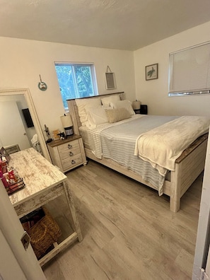Een slaapkamer met een bed, een dressoir, een spiegel en een raam.
