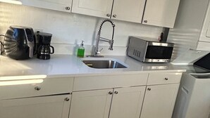 A modern kitchen with white cabinets, a stainless steel sink, a coffee maker, a microwave, and a dishwasher. - Bright, Cozy Home Close to Everything. (Fort Lauderdale)
