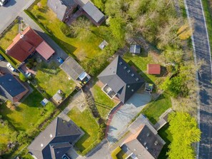 An aerial view of a residential area with multiple houses, some with sloped roofs, surrounded by greenery and a road. - 1 "coastal Child" (St. Peter-Ording)