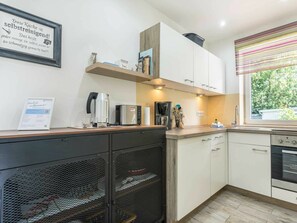 A modern kitchen with white cabinets, a coffee machine, a kettle, and a window with a view of greenery. - 1 "coastal Child" (St. Peter-Ording)
