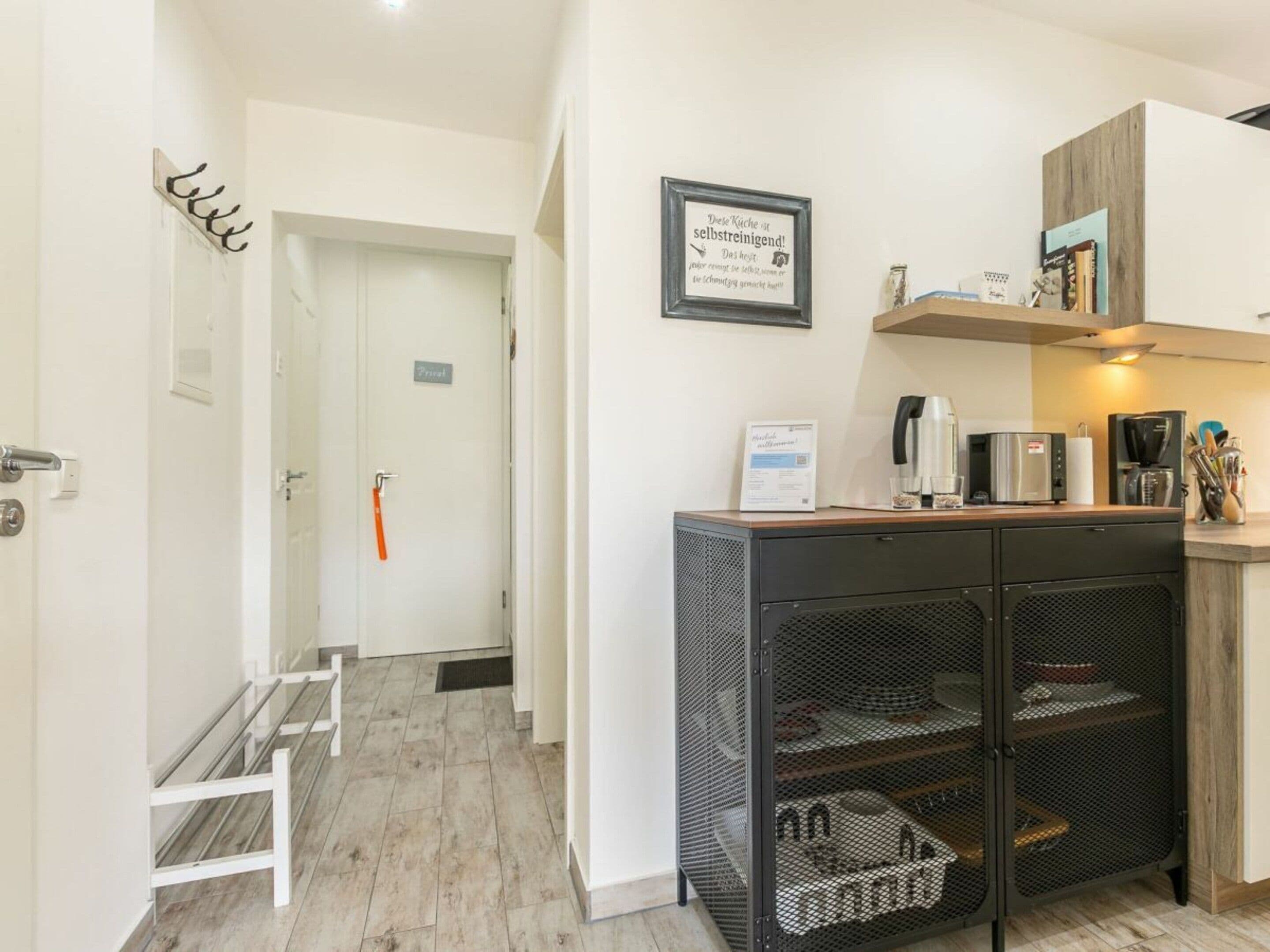 A modern kitchen with a coffee machine, a microwave, and a toaster. There is a small shelf with books and a framed sign on the wall.