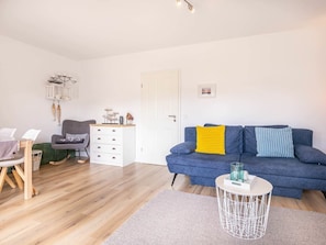 A living room with a blue sofa, a white sideboard, a grey armchair, and a wooden dining table. - 1 "coastal Child" (St. Peter-Ording)