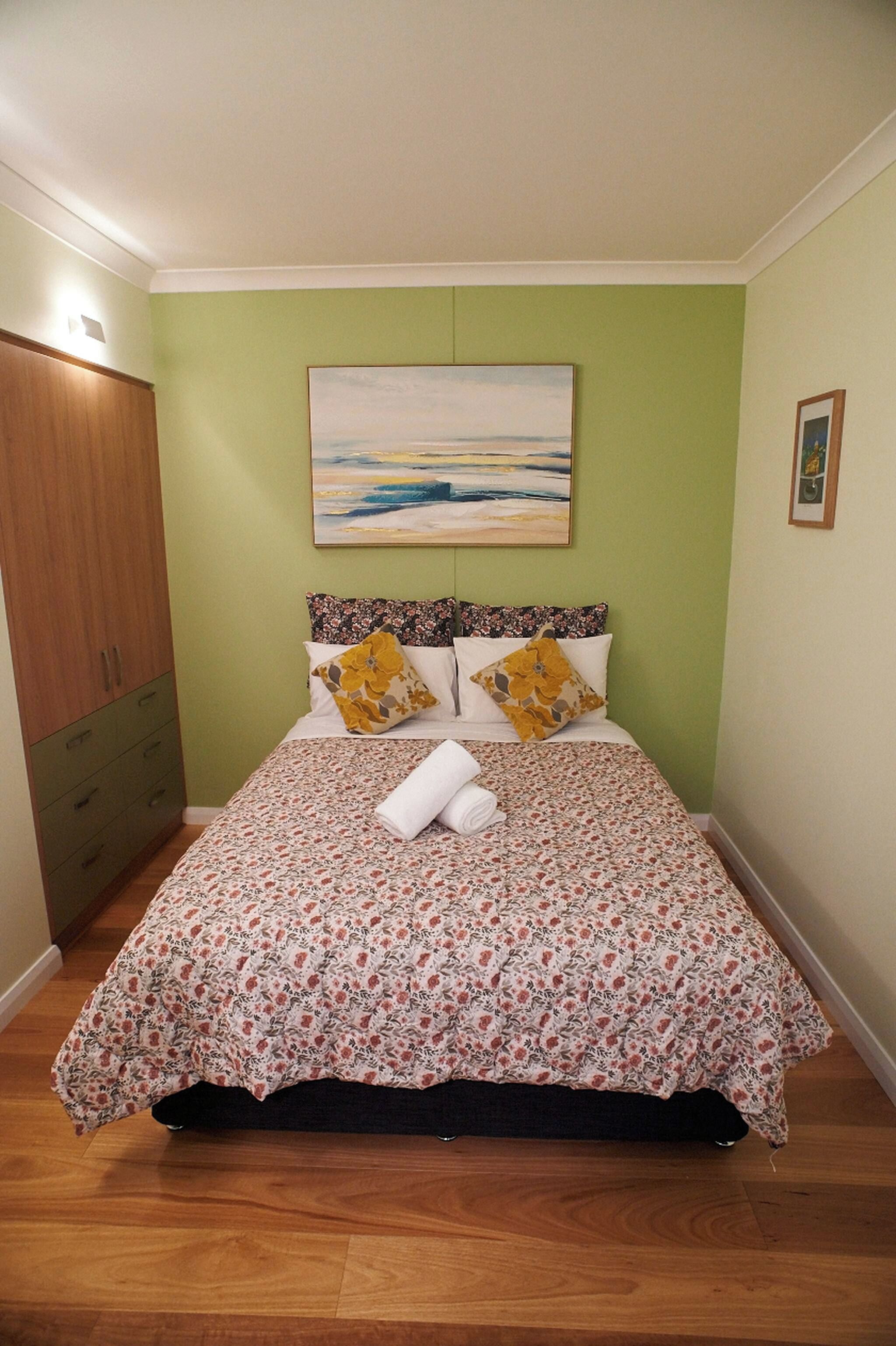 A bedroom with a bed, a painting, a wardrobe, and a small picture on the wall.