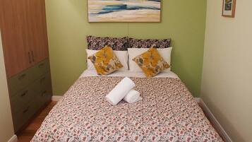 A bedroom with a bed, a painting, a wardrobe, and a small picture on the wall.