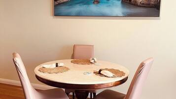 A dining area with a round table, four chairs, and a painting of a coastal landscape.