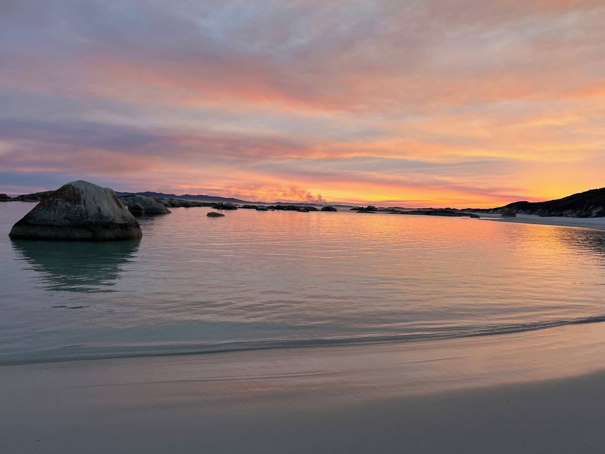 A beach with calm waters and large rocks.