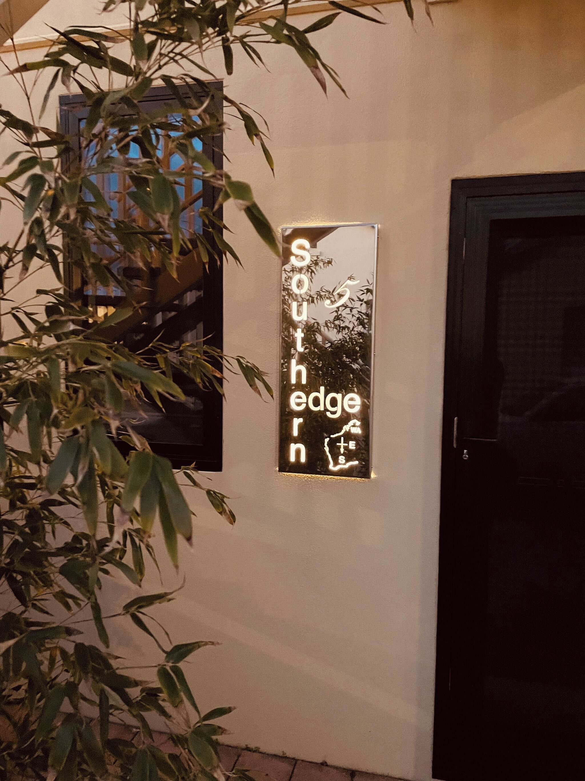 A sign with the text 'South Edge Inn' mounted on a wall, with a door to the right and a window above it.