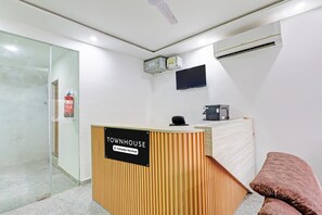 Ein Empfangsbereich mit einem hölzernen Empfangstresen, einem an der Wand befestigten Flachbildfernseher und einem Feuerlöscher links.