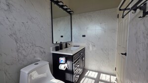 A bathroom with a toilet, sink, mirror, and marble walls. - Cedar Grove 4BR Hillview Retreat (Ogees)