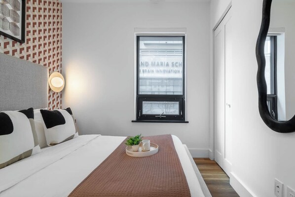 Un dormitorio con cama, una mesita de noche con una planta, una ventana y un espejo en la pared.