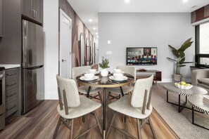Una cocina moderna con un refrigerador de acero inoxidable, una zona de comedor con una mesa redonda dispuesta para cuatro personas y un televisor de pantalla plana montado en la pared.