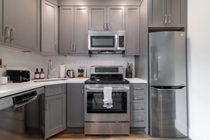 Una cocina moderna con armarios grises, un microondas de acero inoxidable, horno empotrado, lavavajillas y refrigerador.