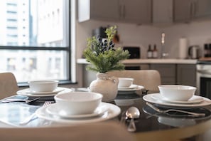 A dining table set with white plates, bowls, and cutlery, with a decorative plant in a ceramic pot.