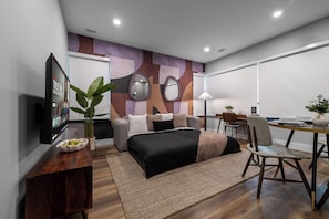 A modern hotel room with a bed, bedside table, TV, and a desk with a chair.