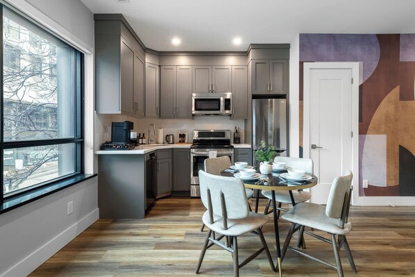 A modern kitchen with grey cabinets, stainless steel appliances, and a dining area with white chairs.