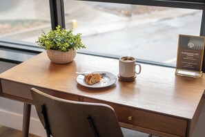 A wooden desk with a plate of food, a cup of coffee, a small potted plant, and a sign offering complimentary WiFi access.