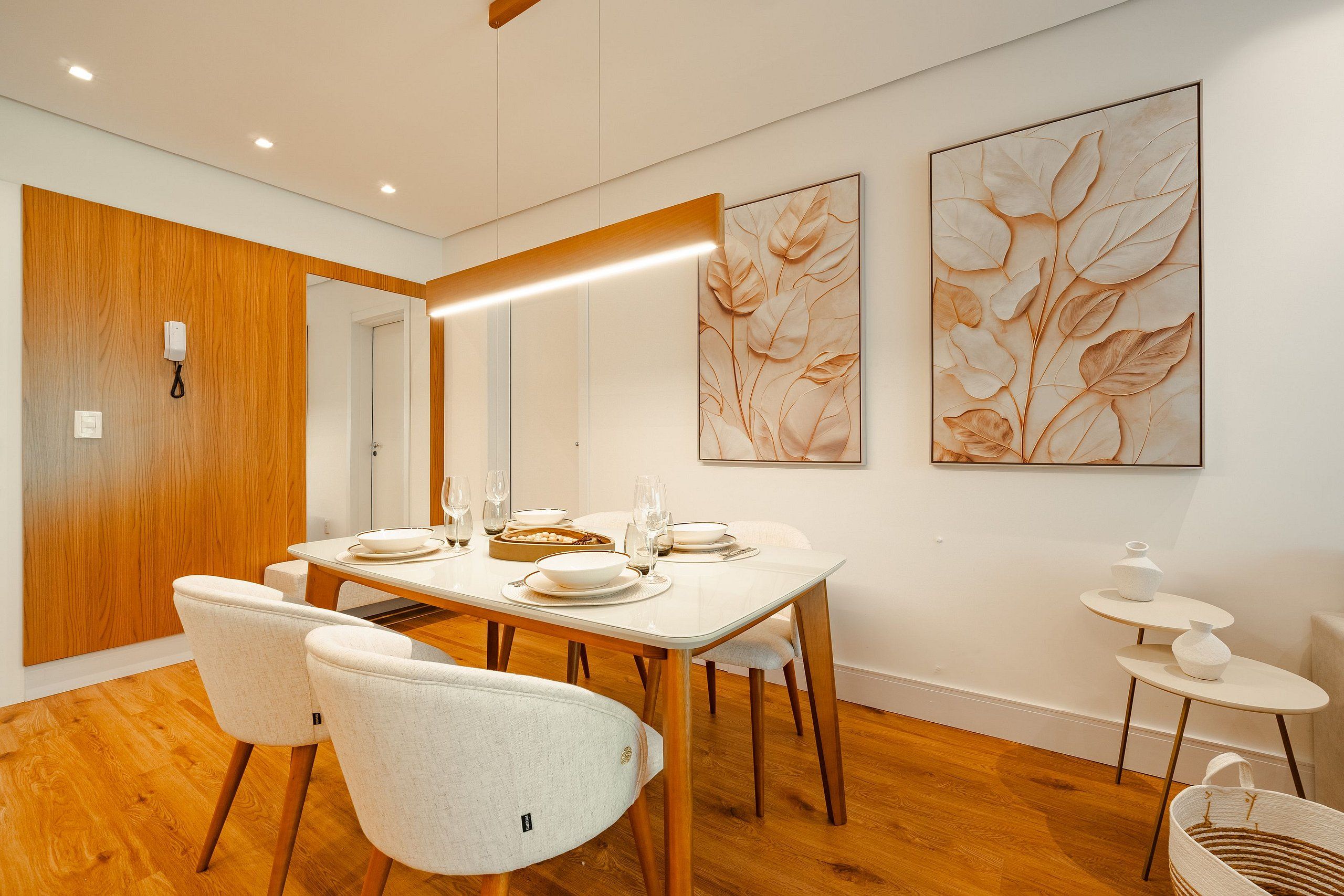 A modern dining area with a wooden dining table set for four, white chairs, and two large floral paintings on the wall.