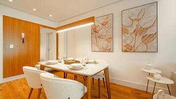 A modern dining area with a wooden dining table set for four, white chairs, and two large floral paintings on the wall.