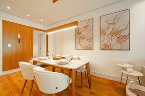 A modern dining area with a wooden dining table set for four, white chairs, and two large floral paintings on the wall. - Vêneto Padova 306 (Gramado)