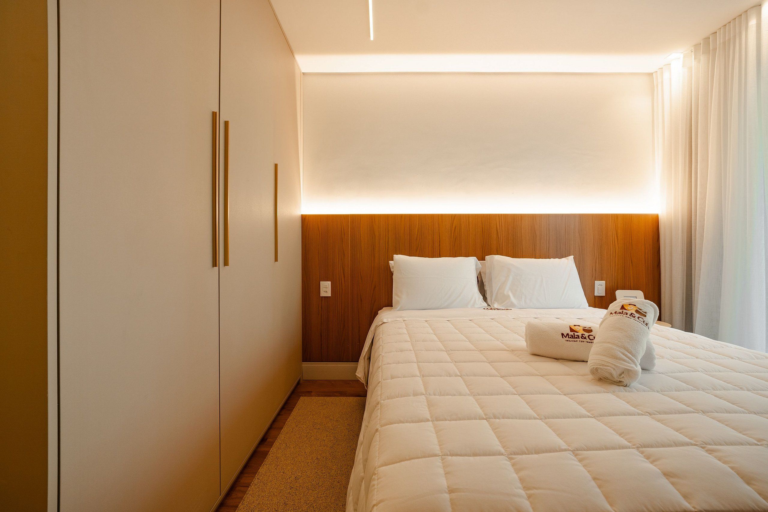 Habitación de hotel con cama, cabecera de madera, ropa de cama blanca y una mesita de noche.