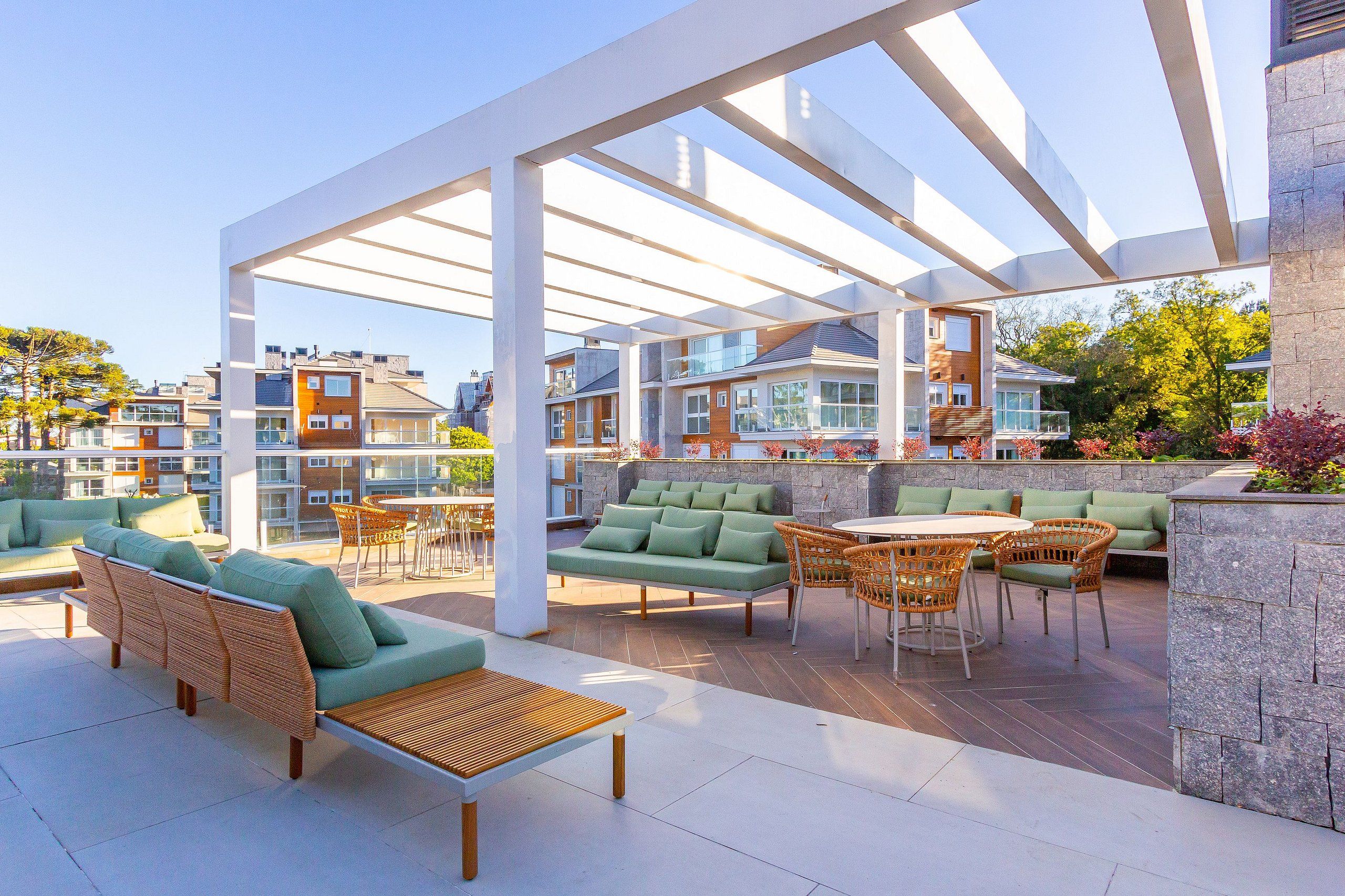 An outdoor patio area with seating arrangements, including sofas and chairs, and a pergola structure providing shade.