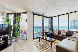 A living room with a TV, sofa, coffee table, and potted plants. - Sunbird 1107e (Panama City Beach)