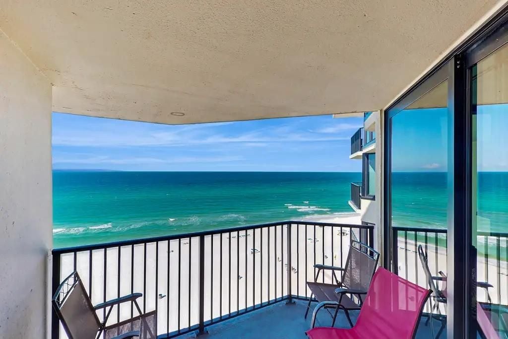 A balcony with a view of the ocean, a railing, and two chairs.