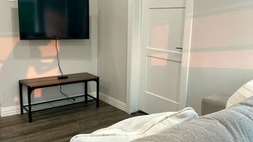 A living room with a flat-screen TV mounted on the wall, a wooden coffee table, a grey sofa, and a white door.