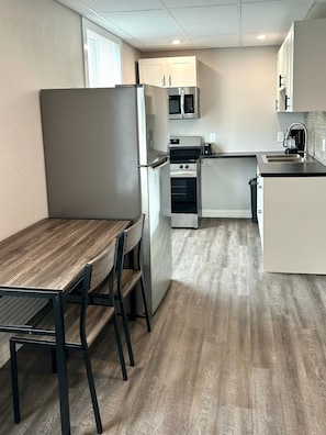 A compact kitchen with a dining area, featuring a refrigerator, microwave, oven, and a sink.