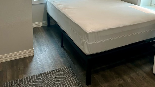 Une chambre avec un lit simple, une fenêtre avec des stores, un plafond doté d’un éclairage encastré et un tapis à motifs sur le sol.