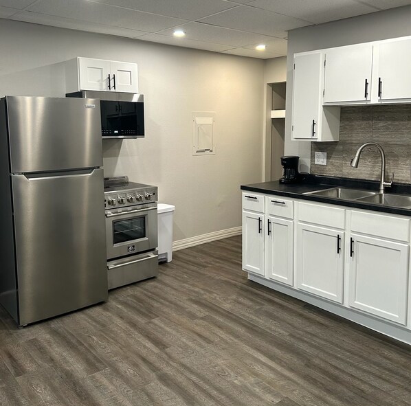 A modern kitchen with stainless steel appliances, white cabinetry, and a black countertop.