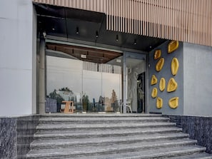 Ein moderner Hauseingang mit Glastür, Marmorstufen und einer Wand mit geometrischen, gelben Verzierungen.