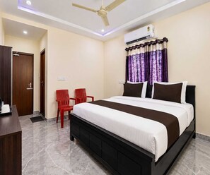 Un dormitorio con cama, escritorio, dos sillas, unidad de aire acondicionado y ventilador de techo.