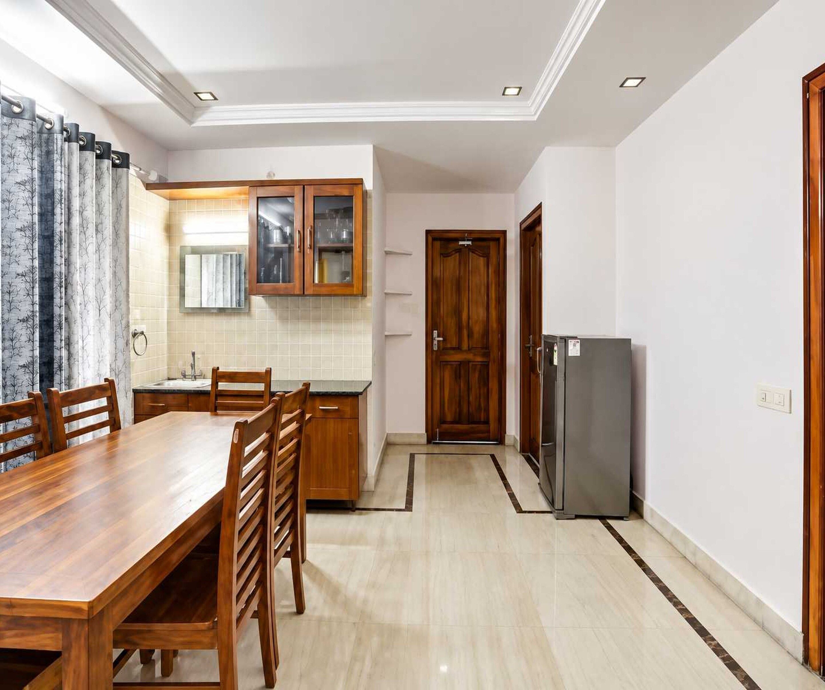 A modern kitchen with a dining area, wooden cabinets, and a refrigerator.