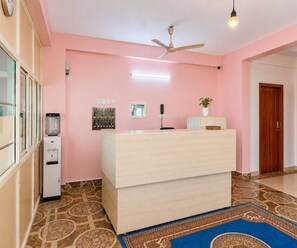 Habitación con mostrador de recepción, ventilador de techo, dispensador de agua, ventana y baldosas de suelo estampadas.