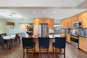 Una cocina moderna con una isla central, armarios de madera, electrodomésticos de acero inoxidable y un comedor con mesa y sillas.