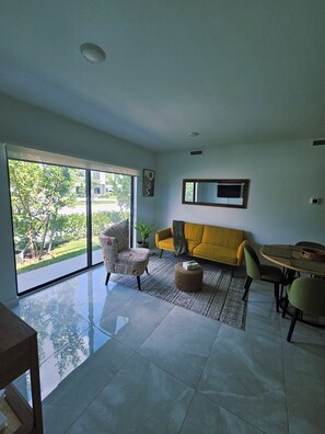 A modern living room with a yellow sofa, a glass door leading to a balcony, and a dining area with a table and chairs. - Modern & Sleek 1-bedroom apartment (Homestead)