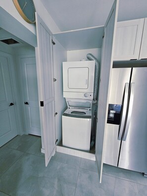 A compact kitchen with a built-in washer and dryer, a stainless steel refrigerator, and a white door. - Modern & Sleek 1-bedroom apartment (Homestead)