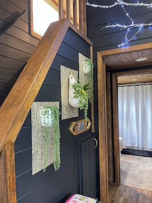 A staircase with a wooden handrail, a wall-mounted decorative panel with greenery, and a door with a sign. - Where peace meets the pines!! Pond fishing, fire pit & egg chairs! (Boaz)