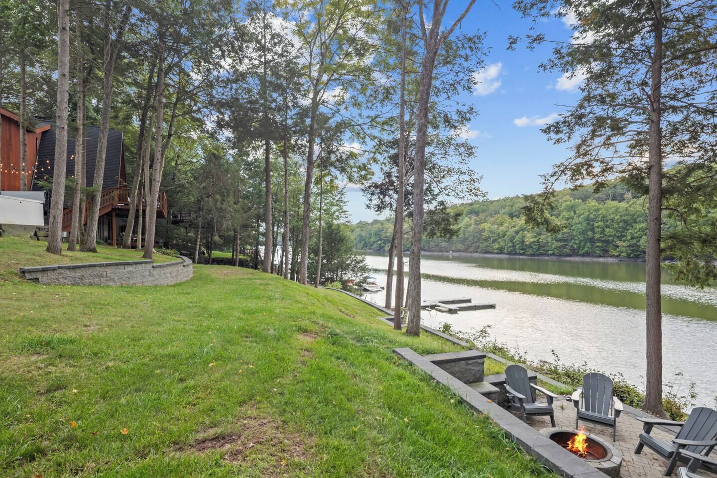 A lakeside property with a fire pit and outdoor seating, surrounded by trees and a view of the lake.