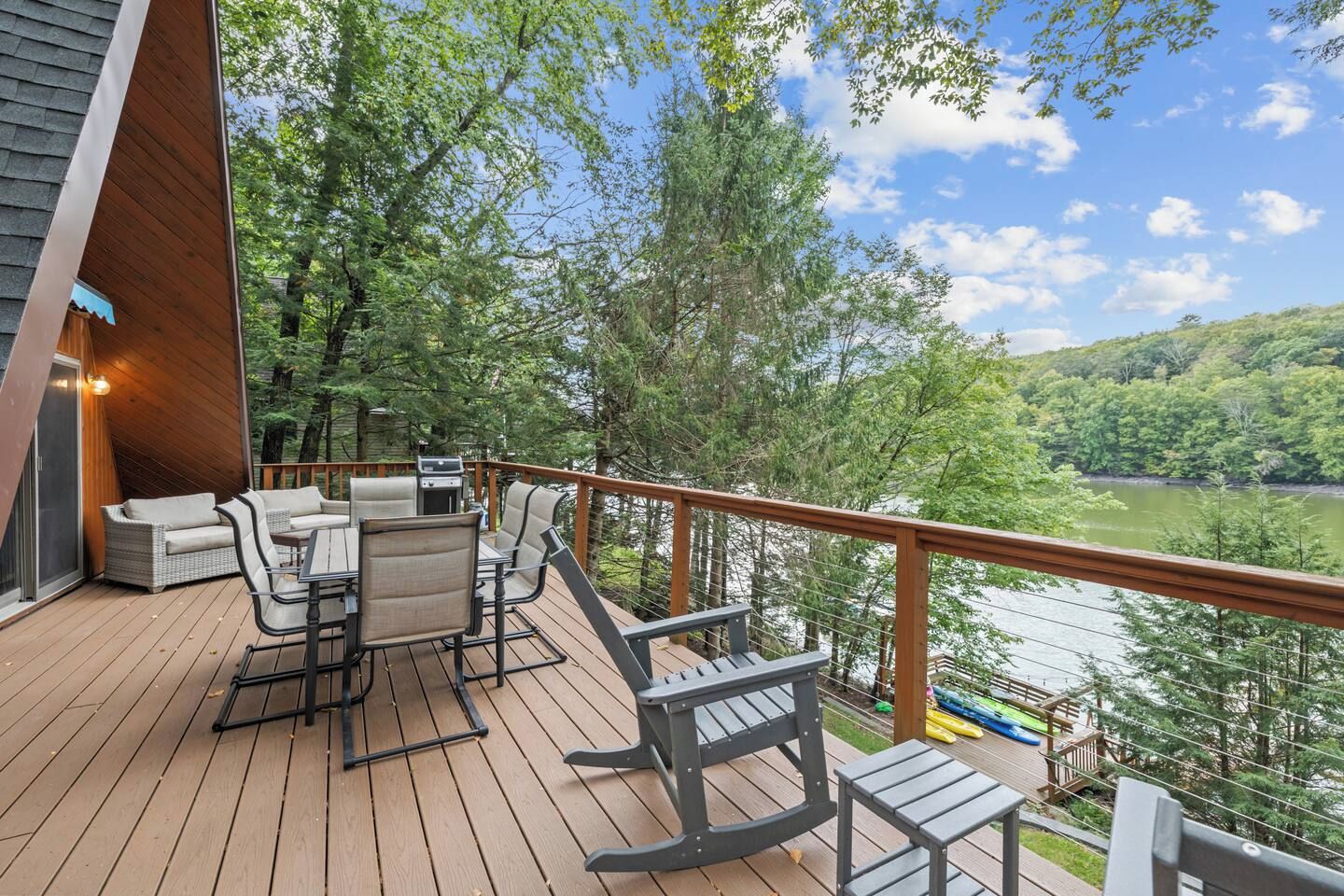 A deck with outdoor furniture, a grill, and a view of a lake surrounded by trees.