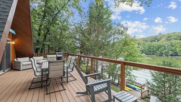 A deck with outdoor furniture, a grill, and a view of a lake surrounded by trees.