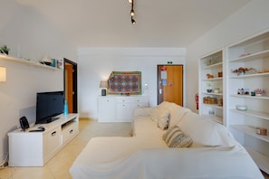 Quarto de hotel moderno com televisão de tela plana, sofá branco, um pequeno armário e estante.