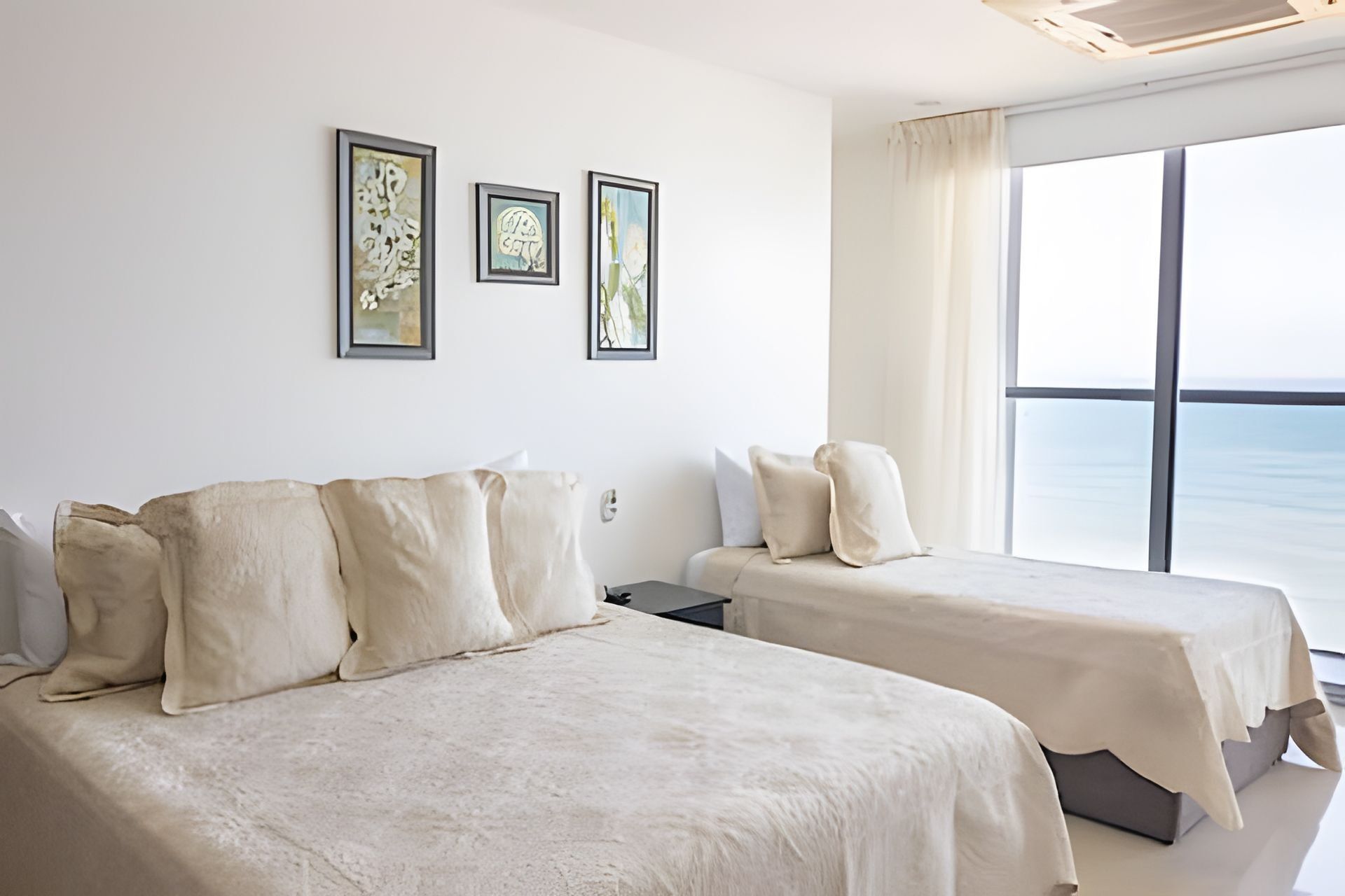 Una habitación de hotel moderna con dos camas, un ventanal con vistas al mar y tres cuadros enmarcados en la pared.